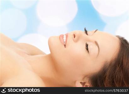beauty, people and health concept - beautiful young woman lying with closed eyes over blue lights background