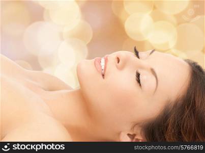 beauty, people and health concept - beautiful young woman lying with closed eyes over beige lights background