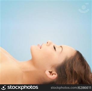beauty, people and health concept - beautiful young woman lying with closed eyes over blue background