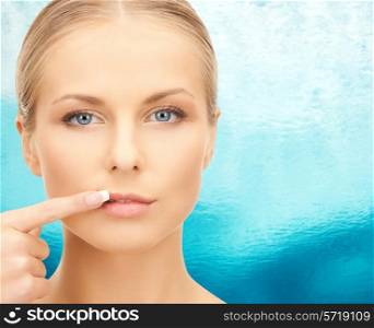 beauty, people and health concept - beautiful young woman pointing finger to her lips over blue ripple water background