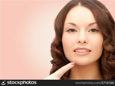 beauty, people and health concept - beautiful young woman pointing finger to her chin over pink background