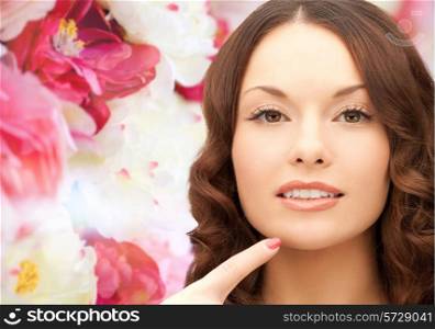 beauty, people and health concept - beautiful young woman pointing finger to her chin over pink floral background