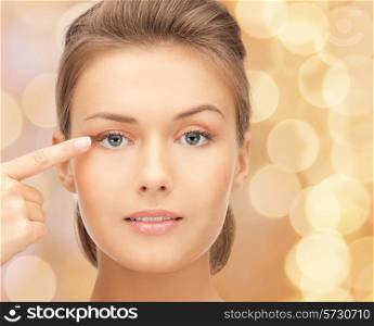 beauty, people and health concept - beautiful young woman pointing finger to her eye over beige lights background