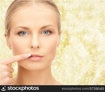 beauty, people and health concept - beautiful young woman pointing finger to her lips over yellow lights background