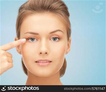 beauty, people and health concept - beautiful young woman pointing finger to her eye over blue background