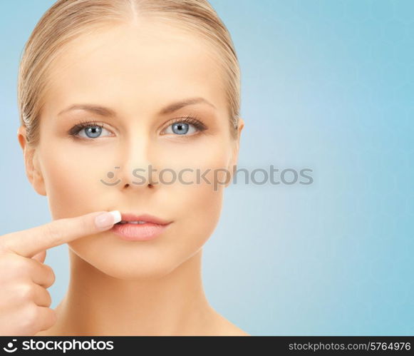 beauty, people and health concept - beautiful young woman pointing finger to her lips over blue background