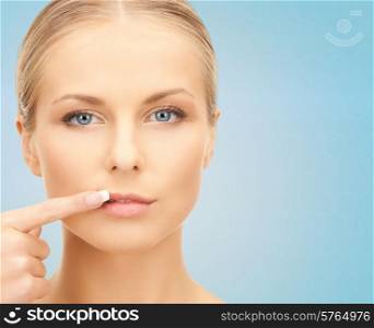 beauty, people and health concept - beautiful young woman pointing finger to her lips over blue background