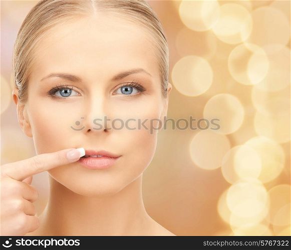 beauty, people and health concept - beautiful young woman pointing finger to her lips over beige lights background