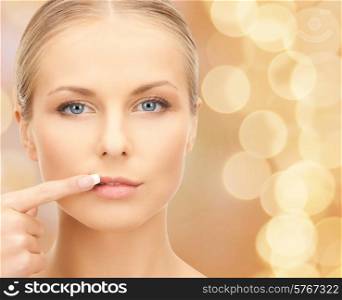 beauty, people and health concept - beautiful young woman pointing finger to her lips over beige lights background