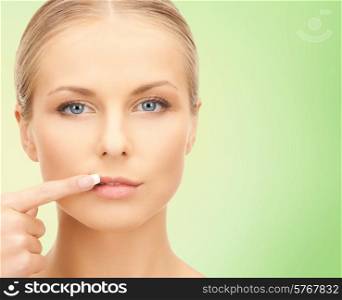 beauty, people and health concept - beautiful young woman pointing finger to her lips over green background