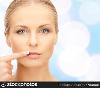 beauty, people and health concept - beautiful young woman pointing finger to her lips over blue lights background