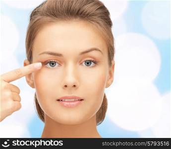 beauty, people and health concept - beautiful young woman pointing finger to her eye over blue lights background