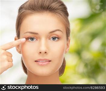 beauty, people and health concept - beautiful young woman pointing finger to her eye over green background