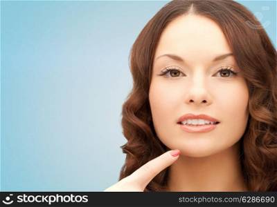 beauty, people and health concept - beautiful young woman pointing finger to her chin over blue background