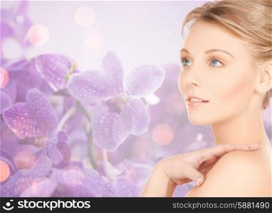 beauty, people and health concept - beautiful young woman touching bare shoulder over purple orchid flowers background