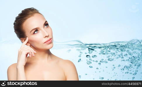 beauty, people and health concept - beautiful young woman touching her face over water splash bubbles on blue background