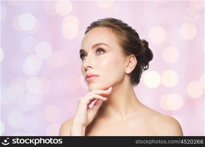 beauty, people and health concept - beautiful young woman touching her face over rose quartz and serenity lights background
