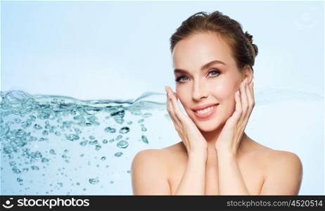 beauty, people and health concept - beautiful young woman touching her face over water splash bubbles on blue background