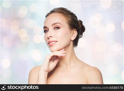 beauty, people and health concept - beautiful young woman touching her face over blue holidays lights background