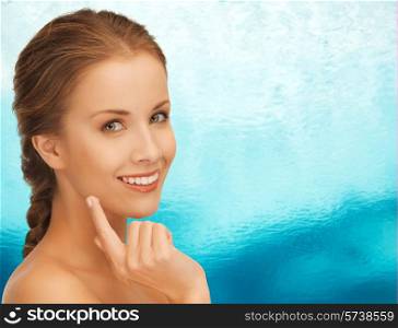 beauty, people and health concept - beautiful young woman touching her face over blue ripple water background
