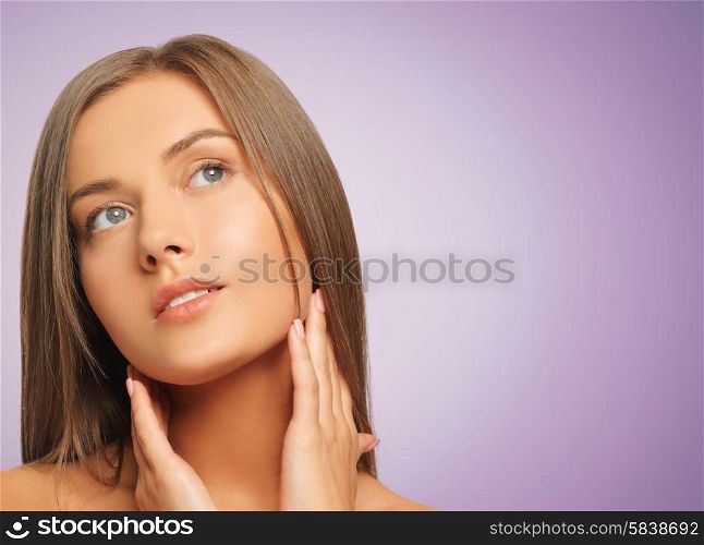 beauty, people and health concept - beautiful young woman touching her face and neck over violet background