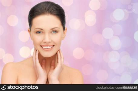 beauty, people and health concept - beautiful young woman touching her face and neck over pink holidays lights background