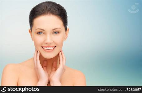 beauty, people and health concept - beautiful young woman touching her face and neck over blue background