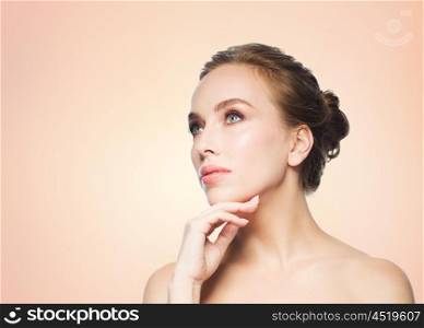 beauty, people and health concept - beautiful young woman touching her face over beige background