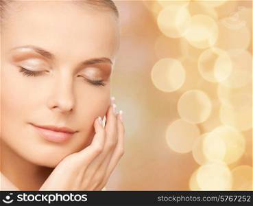 beauty, people and health concept - beautiful young woman touching her face over beige lights background