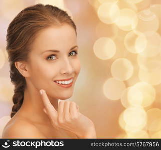 beauty, people and health concept - beautiful young woman touching her face over beige lights background