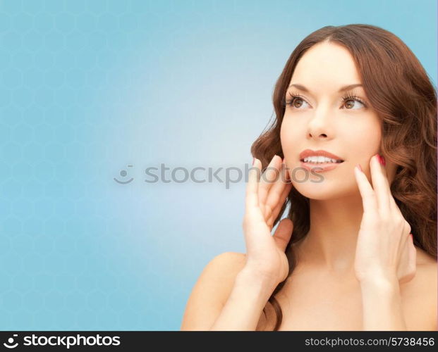 beauty, people and health concept - beautiful young woman touching her face over blue background