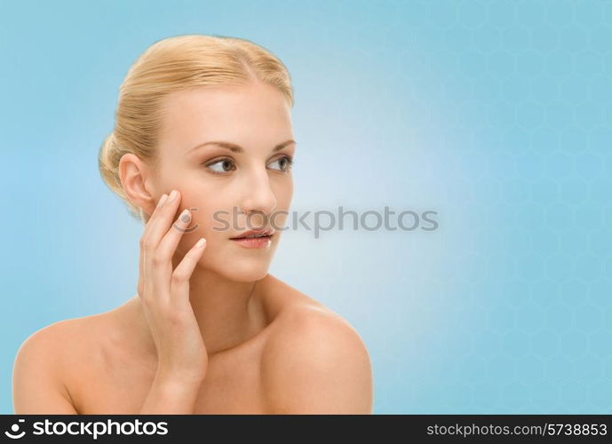 beauty, people and health concept - beautiful young woman touching her face over blue background