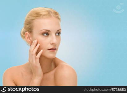 beauty, people and health concept - beautiful young woman touching her face over blue background