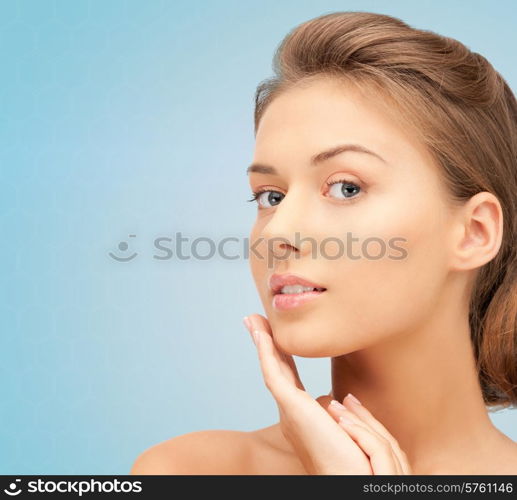 beauty, people and health concept - beautiful young woman touching her face over blue background