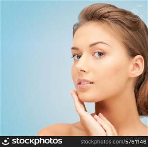 beauty, people and health concept - beautiful young woman touching her face over blue background