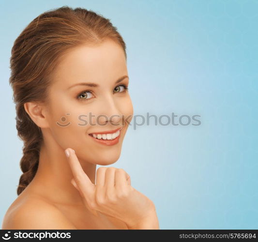 beauty, people and health concept - beautiful young woman touching her face over blue background