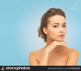 beauty, people and health concept - beautiful young woman touching her face over blue background