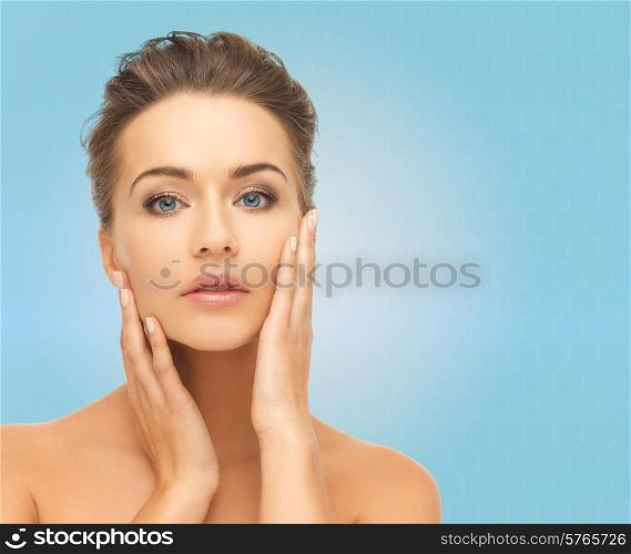 beauty, people and health concept - beautiful young woman touching her face over blue background