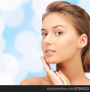beauty, people and health concept - beautiful young woman touching her face over blue lights background
