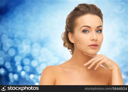 beauty, people and health concept - beautiful young woman touching her face over blue lights background