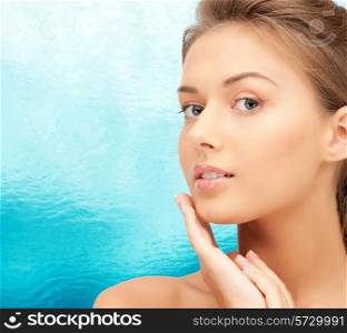 beauty, people and health concept - beautiful young woman touching her face over blue water background