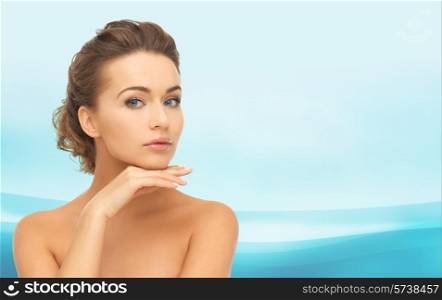 beauty, people and health concept - beautiful young woman touching her face over blue waves background