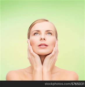 beauty, people and health concept - beautiful young woman touching her face over green background