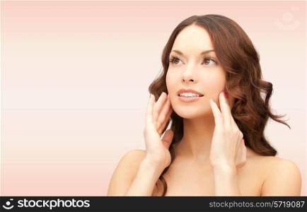 beauty, people and health concept - beautiful young woman touching her face over pink background