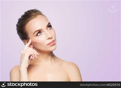 beauty, people and health concept - beautiful young woman touching her face over violet background