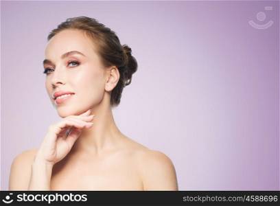 beauty, people and health concept - beautiful young woman touching her face over violet background