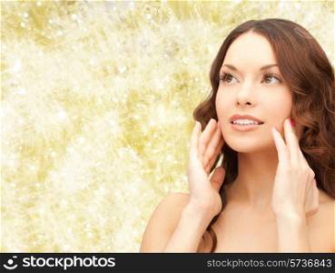 beauty, people and health concept - beautiful young woman touching her face over yellow lights background