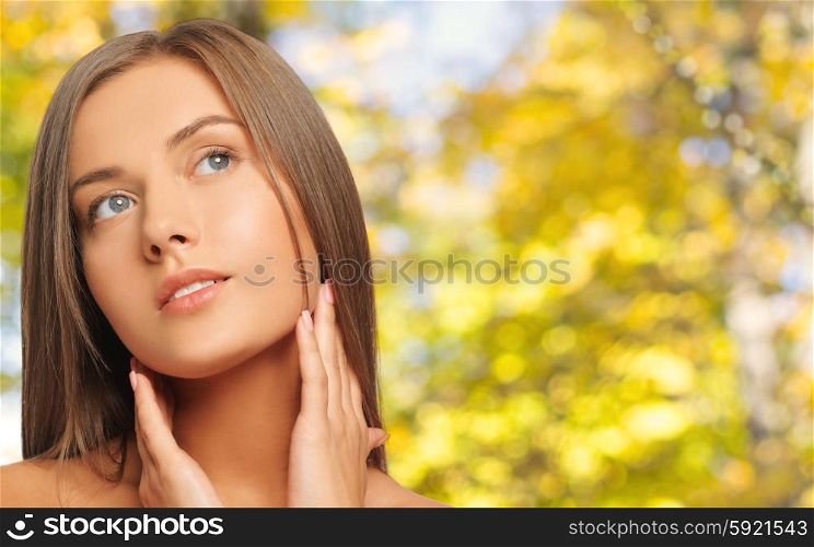 beauty, people and health concept - beautiful young woman touching her neck over yellow autumn background