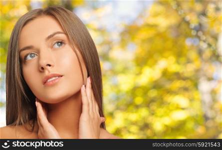beauty, people and health concept - beautiful young woman touching her neck over yellow autumn background