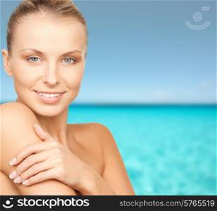beauty, people and health concept - beautiful young woman with bare shoulders over blue water and sky background